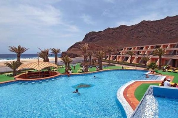 Ein Resort mit großen Pool, umgeben von Palmen und Liegestühlen, liegt in einer Küstenlandschaft mit Bergen und Blick auf das Meer. Ein Resort mit großen Pool, umgeben von Palmen und Liegestühlen, liegt in einer Küstenlandschaft mit Bergen und Blick auf das Meer.