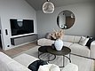 Modernes, stilvolles Wohnzimmer in Südwest-Norwegen: Helle, beige Sofas, runder Couchtisch mit Dekoration, großer Fernseher und runder Spiegel an grauen Wänden. Perfekt für gemütliche Entspannung im skandinavischen Design. Keywords: Skandinavisches Wohnzimmer, modernes Interieur.