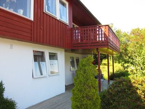 Rotes Holzhaus mit Balkon und umliegendem Garten in der Region Hitra, Norwegen. Ideal für Angelurlaub mit Aussicht auf malerische Natur und entspannte Stunden. Perfekte Unterkunft für Angler und Naturliebhaber.