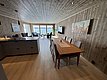 Moderne, gemütliche Ferienwohnung auf Hitra, Norwegen. Holzvertäfelte Wände, Essbereich mit großem Tisch, Blick auf das Meer durch große Fenster. Ideal für komfortablen Angelurlaub. Hochwertige Ausstattung, naturnahe Umgebung, perfekt für Erholung und Abenteuer.