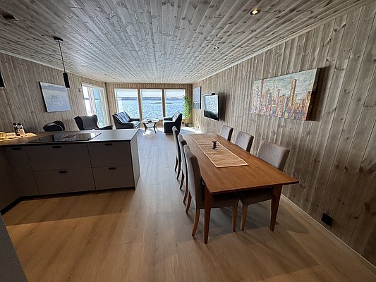 Moderne, gemütliche Ferienwohnung auf Hitra, Norwegen. Holzvertäfelte Wände, Essbereich mit großem Tisch, Blick auf das Meer durch große Fenster. Ideal für komfortablen Angelurlaub. Hochwertige Ausstattung, naturnahe Umgebung, perfekt für Erholung und Abenteuer.