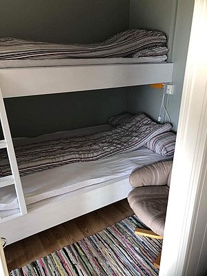 Gemütliches Zimmer mit Etagenbett und Sessel, perfekt zum Entspannen nach einem Angeltag in Nordland, Norwegen. Geschmackvoll eingerichtet mit buntem Teppich und heller Bettwäsche bietet es komfortable Unterkunft für zwei Personen.