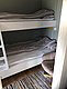 Gemütliches Zimmer mit Etagenbett und Sessel, perfekt zum Entspannen nach einem Angeltag in Nordland, Norwegen. Geschmackvoll eingerichtet mit buntem Teppich und heller Bettwäsche bietet es komfortable Unterkunft für zwei Personen.