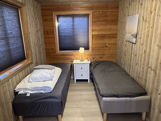Holzgetäfeltes Schlafzimmer in Norwegen mit zwei Einzelbetten, schlichtem Nachttisch und Lampe. Ideal für entspannenden Angelurlaub in Hitra, um die Ruhe und Natur zu genießen. Perfekt für Abenteuer in skandinavischer Gemütlichkeit.