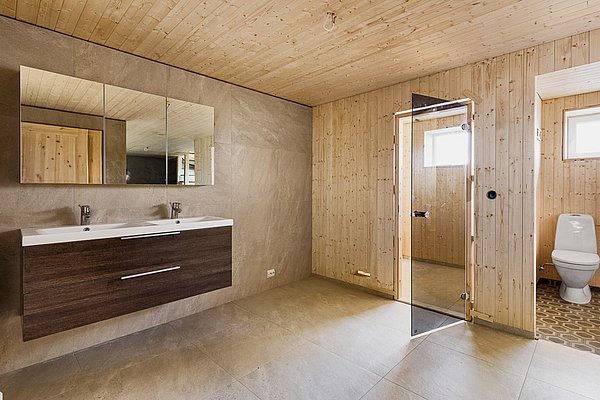 Ein modernes Badezimmer aus Holz in Nordland, Norwegen. Doppelte Waschbecken, Glasdusche, helle Fliesen und natürliche Holzverkleidung sorgen für ein helles, einladendes Ambiente. Perfekt für einen erholsamen Angelurlaub im skandinavischen Stil.
