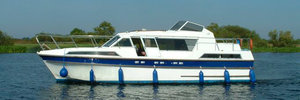 Ein weißes Hausboot fährt auf dem River Shannon in Irland. Es ist mit blauen Fendern ausgestattet. Umgeben von grüner Uferlandschaft bietet die Region ideale Bedingungen für Angelreisen und entspannte Bootstouren.