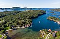 Luftaufnahme der malerischen Küstenlandschaft von Hitra, Norwegen: Sattgrüne Wälder, klares blaues Wasser, idyllische Küstenhäuser. Perfekte Kulisse für Angelurlaub und Outdoor-Abenteuer. Entdecke unberührte Natur und reiche Fischgründe.