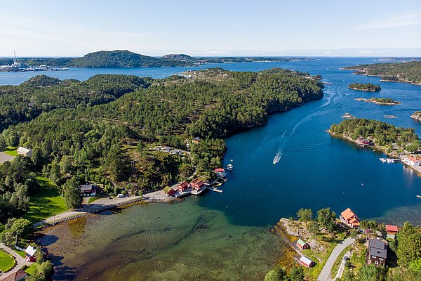Luftaufnahme der malerischen Küstenlandschaft von Hitra, Norwegen: Sattgrüne Wälder, klares blaues Wasser, idyllische Küstenhäuser. Perfekte Kulisse für Angelurlaub und Outdoor-Abenteuer. Entdecke unberührte Natur und reiche Fischgründe.