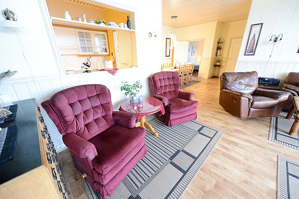 Gemütliches Wohnzimmer in Nord-Norwegen mit roten Sesseln, Ledersessel und Holzboden, idealer Rückzugsort nach einem Angeltag. Perfekt für Entspannung und gemeinsame Abende nach erfolgreichen Angelausflügen in der malerischen Region.