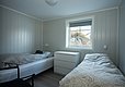 Gemütliches Schlafzimmer in Hitra, Norwegen. Zwei Einzelbetten, helle Holzwände, Fenster mit Blick auf Natur. Perfekt für Angelreisende, die nach Entspannung und Komfort nach einem erfolgreichen Angeltag suchen.