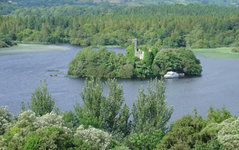Eine bewaldete Insel mit einer alten Ruine und einem Boot in einem ruhigen See, umgeben von dichten Wäldern.