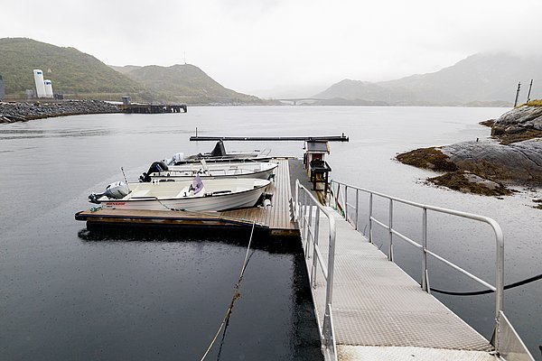 Ein ruhiger Hafen in Nordland, Norwegen, mit angedockten Fischerbooten, umgeben von malerischen Bergen und nebligem Himmel – ein idealer Ausgangspunkt für einen abenteuerlichen Angelurlaub.