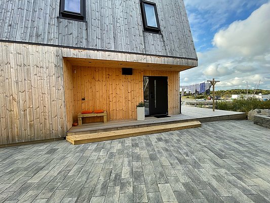 Moderner Holzbau in Hitra, Norwegen: Schlichtes Design mit hölzerner Fassade, Steinweg und einladender Veranda. Ruhige Umgebung, ideal für entspannte Angelreisen in skandinavischem Flair. Petri Heil!