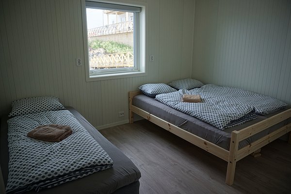 Gemütliches Schlafzimmer in Nordland, Norwegen mit zwei Betten, Fensterblick auf Holzterrasse und Wald. Ideal für erholsame Angelreisen, bietet Komfort und Ruhe in skandinavischem Design. Perfekt für einzigartige Erlebnisse in der Natur.