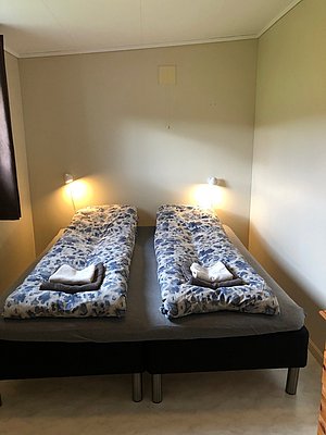 Gemütliches Schlafzimmer in Nord-Norwegen mit zwei Einzelbetten, blauen Bettdecken und weichen Handtüchern. Perfekt für Erholung nach einem erlebnisreichen Angelurlaub in malerischer Landschaft. Einladende Beleuchtung sorgt für eine warme Atmosphäre.