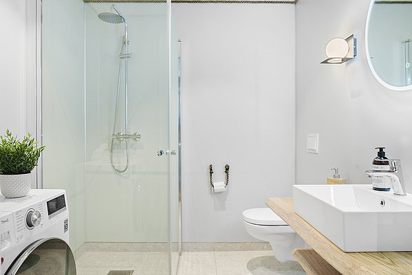 Modernes Badezimmer in Südwest-Norwegen mit Dusche, Waschmaschine und stilvoller Einrichtung. Helle Farben, runde Spiegel, Holzdetails und Pflanzen sorgen für entspannte Atmosphäre. Ideal für komfortable Angelreisen.