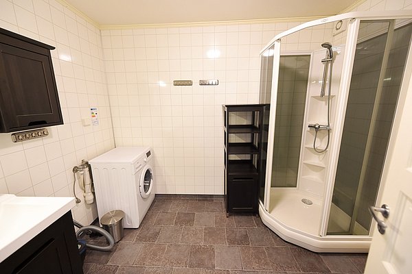 Modernes Badezimmer in Hitra, Norwegen mit Dusche, Waschmaschine und Schrank auf Fliesenboden. Ideal für komfortable Angelurlaube. Skandinavisches Design und praktische Annehmlichkeiten schaffen zusätzliche Bequemlichkeit für Reisende und Angelfreunde.