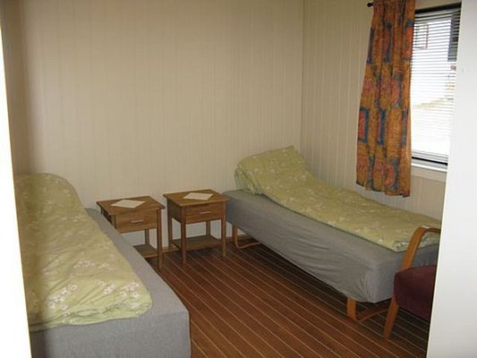 Gemütliches Schlafzimmer in Nordland, Norwegen, mit zwei Einzelbetten, Holzmöbeln und bunten Vorhängen. Perfekt für Angler, die nach einem Abenteuer am Meer entspannen möchten. Ideal für erholsamen Angelurlaub in Skandinavien.