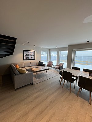 Moderne Ferienwohnung in Nordland, Norwegen: Gemütliches Wohnzimmer mit stilvoller Einrichtung, großem Fenster und Blick aufs Wasser. Ideal für Angelreisen und entspannte Aufenthalte in malerischer Umgebung. Perfekte Mischung aus Komfort und Naturerlebnis.