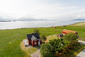 Rotes Haus in Nordland, Norwegen, mit Blick auf fjordähnliche Küstenlandschaft und umliegende Hügel. Idyllische Ruhe und Natur, perfekt für Angelabenteuer und Entspannung. Ideal für Angler und Naturliebhaber.