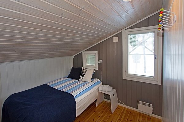 Gemütliches Schlafzimmer in einer nordnorwegischen Hütte mit Holzwänden, Einzelbett, und Dachfenster. Perfekt für Angelreisende auf der Suche nach Ruhe und Komfort in der Natur.