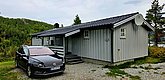 Graues Holzhaus in Norwegens Hitra, umgeben von Waldlandschaft, bietet ideale Unterkunft für Angelurlaub. Im Vordergrund parkt ein Auto; perfekte Basis für Entspannung und Abenteuer in der Natur.
