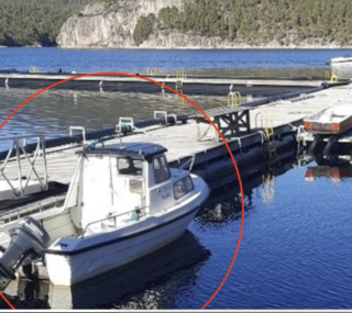 Fischereihafen in Nord-Norwegen: Ein kleines Fischerboot vertäut am Holzsteg mit ruhigem Wasser und bewaldeten Felsen im Hintergrund. Ideal für Angelurlaube voller Abenteuer und beeindruckender Naturerlebnisse.