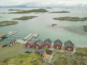 Küstenlandschaft in Nordland, Norwegen: Rotgetäfelte Hütten, klare Gewässer, idyllische Inseln und Stege mit Booten. Ideal für Angelurlaub und Naturliebhaber. Ruhige, malerische Umgebung mit beeindruckendem Fjordblick. Perfekter Startpunkt für ein unvergessliches Angelerlebnis.