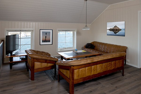 Gemütliches Wohnzimmer mit zwei braunen Ledersofas, einem Flachbildfernseher und einem Fenster mit Meerblick.