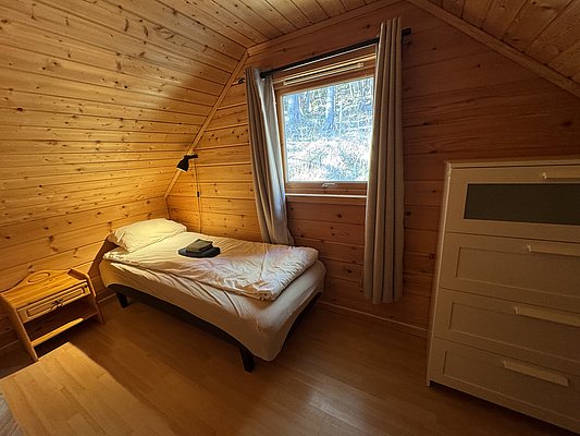 Ein gemütliches Schlafzimmer in einer Holzhütte auf Hitra, Norwegen, bietet Holzverkleidung, ein Einzelbett, einen Nachttisch und einen Ausblick in die Natur. Perfekt für entspannende Angelurlaube.