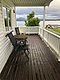 Gemütliche Veranda mit Blick auf einen fjordähnlichen See, schneebedeckte Berge und eine rote Hütte, ideal für Angelreisen in Nord-Norwegen. Perfektes Ambiente für Entspannung und Abenteuer.