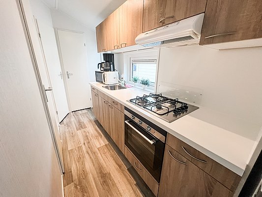 Moderne Küchenzeile in Nord-Norwegen mit Holzschränken, Gasherd und Mikrowelle. Heller Raum mit Laminatboden, ideal für Angelurlauber, die nach Abenteuern in der Natur kulinarische Köstlichkeiten zubereiten möchten. Perfekt ausgestattet für Komfort und Funktionalität.