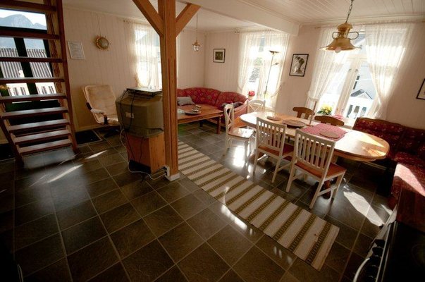 Gemütliches Wohnzimmer in Nord-Norwegen mit Holzmöbeln, Teppich und Tageslicht von großen Fenstern. Perfekt für Entspannung nach einem erfolgreichen Angeltag in malerischer Umgebung. Ideal für Angelurlaub und erholsame Stunden.