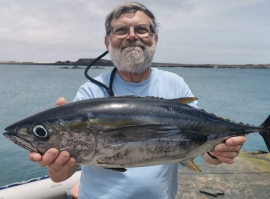 Ein glücklicher Angler präsentiert stolz seinen großen Fischfang am malerischen Ufer von São Vicente, Kapverden. Perfekter Angelurlaub für Abenteurer und Genießer in exotischer Umgebung.