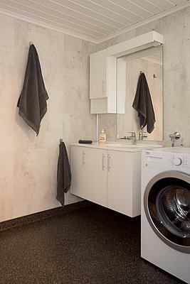 Modernes Badezimmer mit Waschmaschine, weißem Waschbeckenunterschrank mit Spiegel, an dem graue Handtücher hängen.