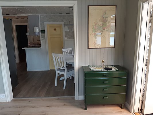 Ein gemütliches, lichtdurchflutetes Zimmer mit Holzboden zeigt einen grünen Schrank unter einer gerahmten Karte, und im Hintergrund sind weiße Möbel und eine gelbe Tür zu sehen.