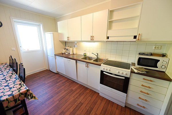 Helle Küche in Hitra, Norwegen: Moderne Ausstattung mit Herd, Mikrowelle, Kühlschrank und Esstisch. Ideal für Angelurlauber, um frischen Fang zuzubereiten. Gemütliche Atmosphäre für einen komfortablen Aufenthalt in atemberaubender Umgebung.
