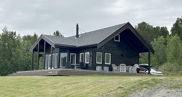 Ein modernes Holzhaus in Nord-Norwegen, umgeben von grünen Bäumen und grauem Himmel, ideal für Angelurlaub und Naturgenuss. Große Fenster bieten herrlichen Ausblick, perfekte Rückzugsort für Entspannung und Erholung.
