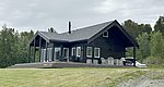 Ein modernes Holzhaus in Nord-Norwegen, umgeben von grünen Bäumen und grauem Himmel, ideal für Angelurlaub und Naturgenuss. Große Fenster bieten herrlichen Ausblick, perfekte Rückzugsort für Entspannung und Erholung.