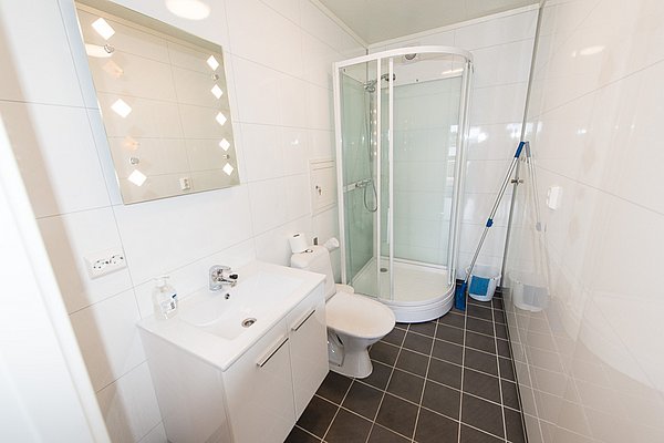 Modernes, weiß gefliestes Badezimmer in Nordland, Norwegen. Ausstattung: runde Duschkabine, Waschbecken, Toilette. Helle, saubere Atmosphäre. Perfekt für Angelurlaube mit komfortabler Unterkunft in der malerischen Region.