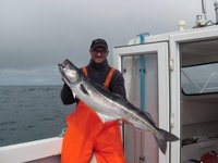Ein Angler in orangefarbener Kleidung steht auf einem Boot und hält einen großen Fisch in den Händen.