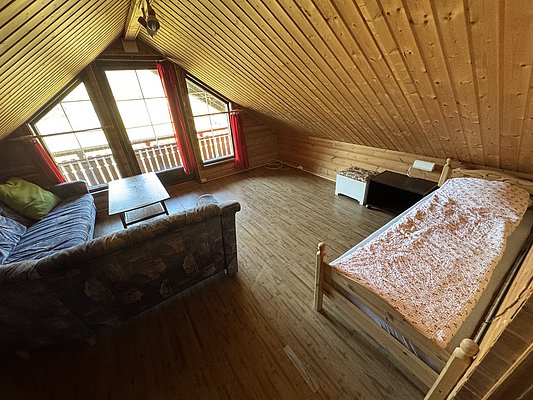 Ein gemütliches Dachzimmer in Hitra, Norwegen, mit Holzverkleidung und großen Fenstern. Blick auf Balkon, Sofa, Bett und Tisch schaffen eine einladende Atmosphäre für entspannte Angelurlaube. Ideal für Ruhe und Erholung.