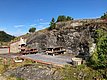Holzterrasse in Hitra, Norwegen, mit rustikalem Außengrill, Holzbänken und imposanter Felskulisse. Perfekt für entspannte Pausen in der idyllischen Natur, umgeben von üppigem Grün und blauem Himmel. Ideal für Angelurlaube.