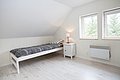 Helles, minimalistisches Schlafzimmer in Nord-Norwegen: Einzelbett mit schwarz-weißem Bettzeug, Nachtisch mit Lampe, zwei Fenster mit Blick auf Bäume. Ideal für einen ruhigen Angelurlaub in skandinavischem Stil.