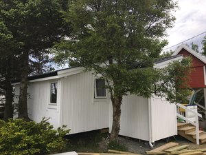 Weiße norwegische Hütte auf Hitra, umgeben von Bäumen. Idealer Angelurlaubsort mit gemütlicher Atmosphäre und Nähe zur Natur. Perfekt für Erholung und Abenteuer in Norwegen.