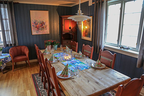 Einladendes, rustikales Esszimmer in Nord-Norwegen mit Holztisch, gemütlicher Beleuchtung und dekorativem Gedeck. Warme Farben und Kunst an den Wänden schaffen eine heimelige Atmosphäre. Perfekt für entspannte Abende nach einem erfolgreichen Angelurlaub.