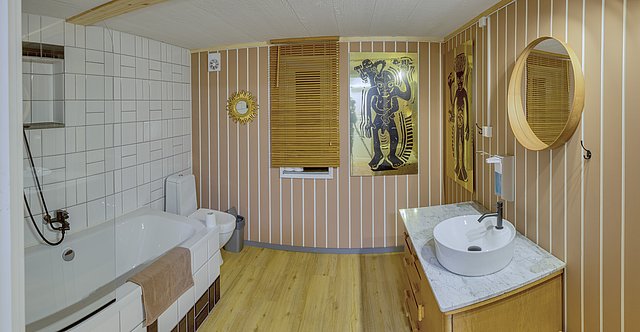 Gemütliches Badezimmer in Nordland, Norwegen: Moderne Einrichtung mit Holzelementen, Badewanne, rundem Spiegel und künstlerischen Wandbildern. Warme, einladende Atmosphäre ideal für Entspannung nach erlebnisreichem Angelabenteuer. Perfekter Rückzugsort im skandinavischen Stil.