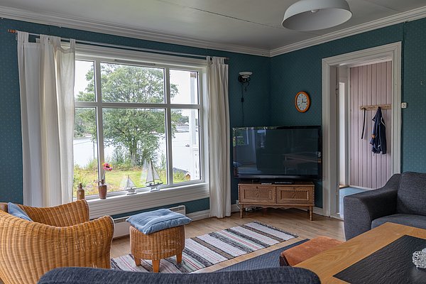 Gemütliches Wohnzimmer in Hitra, Norwegen, mit Blick auf die Natur. Große Fenster, komfortable Sitzecke, Fernseher und dekorative Accessoires schaffen ein behagliches Ambiente – perfekt für entspannende Angelurlaube.