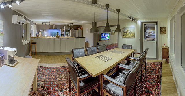 Gemütliches skandinavisches Ferienhaus in Nordland, Norwegen: Geschmackvoll eingerichtetes Esszimmer mit Holztisch, Ledersesseln und Teppich. Moderne Küche im Hintergrund, ideal für Angelurlaub in atemberaubender Naturkulisse.
