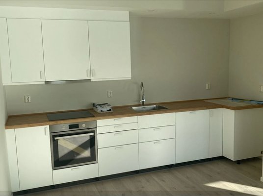 Helle, moderne Einbauküche mit weißen Schränken, Holzarbeitsplatte, Spüle und integriertem Ofen auf hellem Bodenbelag. Helle, moderne Einbauküche mit weißen Schränken, Holzarbeitsplatte, Spüle und integriertem Ofen auf hellem Bodenbelag.